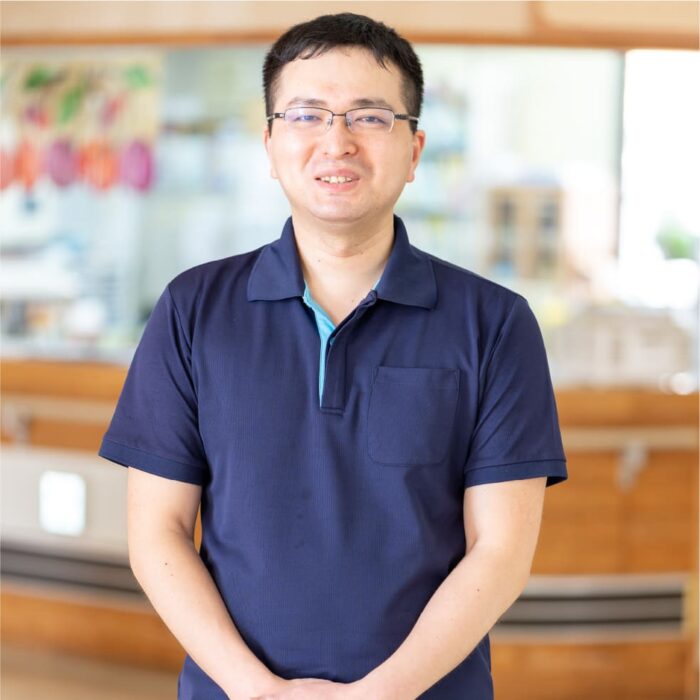 介護施設のスタッフの職業写真。紺色ポロシャツを着た男性職員の笑顔のポートレート。